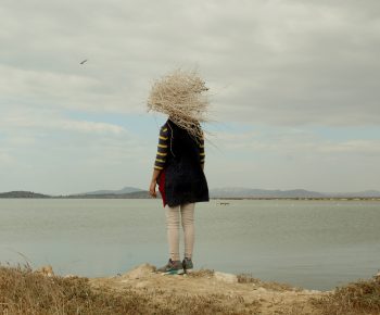 Photographie d'une femme de dos au bord d'un lac avec un amas de branches sur le visage.